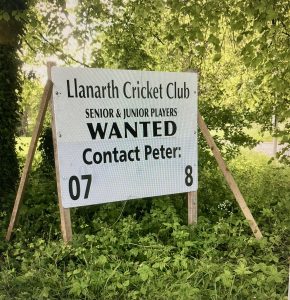 Image of a roadside ad. Black text on a white background that says: Llanarth Cricket Club, Senior and Junior Players. WANTED, Contact Peter and then a phone number which has been hidden.